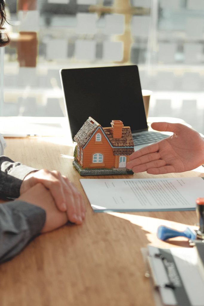 Cliente recibiendo asesoramiento jurídico y legal inmobiliario en una oficina de inmobiliaria, con un modelo de casa sobre la mesa, simbolizando la compra o venta de propiedad
